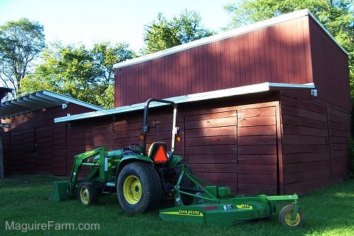 A John Deere tractor in front of the lower red barn