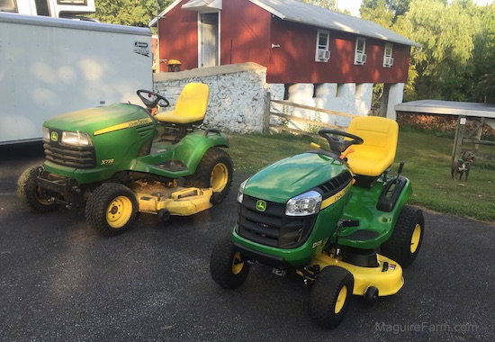 A John Deere X728 Ultimate™ Tractor next to a John Deere D125 mower with a red barn, and a blue nose pit bull terrier dog in the background.